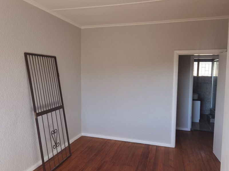 An empty bedroom featuring hardwood flooring and neutral walls, with a doorway leading to an adjacent bathroom area.