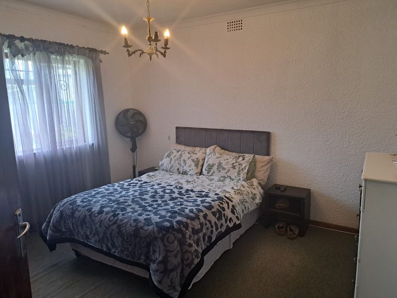 A standard bedroom featuring textured walls, carpeted flooring, and a central chandelier light fixture.