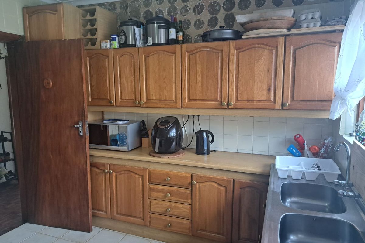 A dated kitchen featuring traditional wooden cabinetry, laminate countertops, and a double stainless steel sink, offering potential for a modern renovation.
