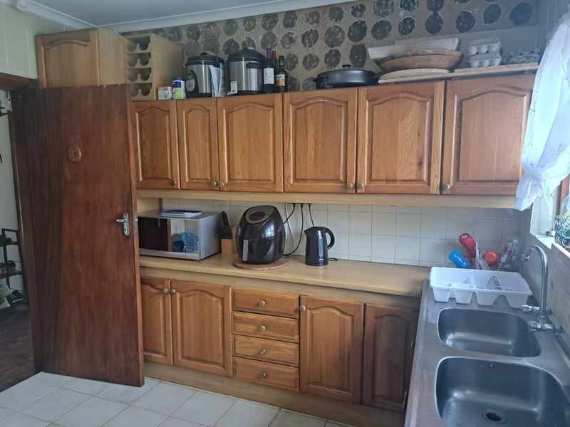 A dated kitchen featuring traditional wooden cabinetry, laminate countertops, and a double stainless steel sink, offering potential for a modern renovation.