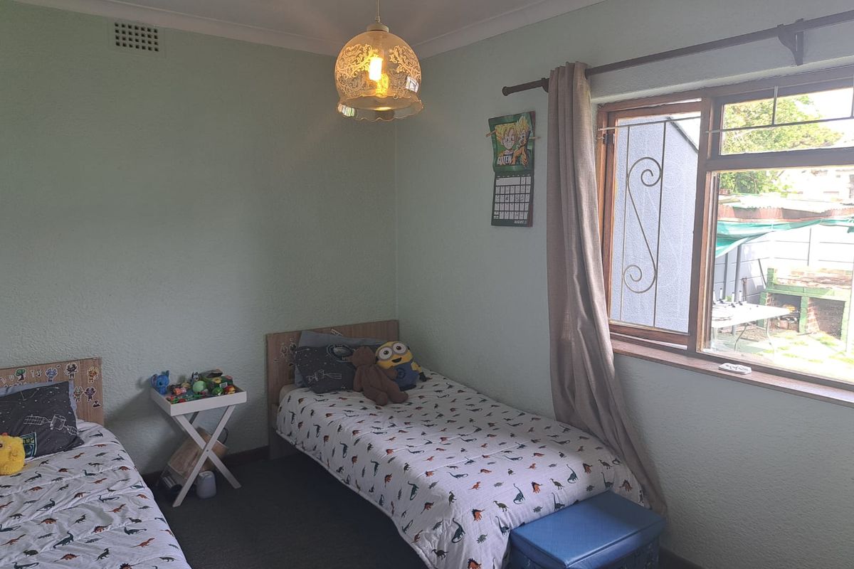 A functional bedroom featuring textured walls, coving, and a timber-framed window with security bars, offering a view of the rear garden area.