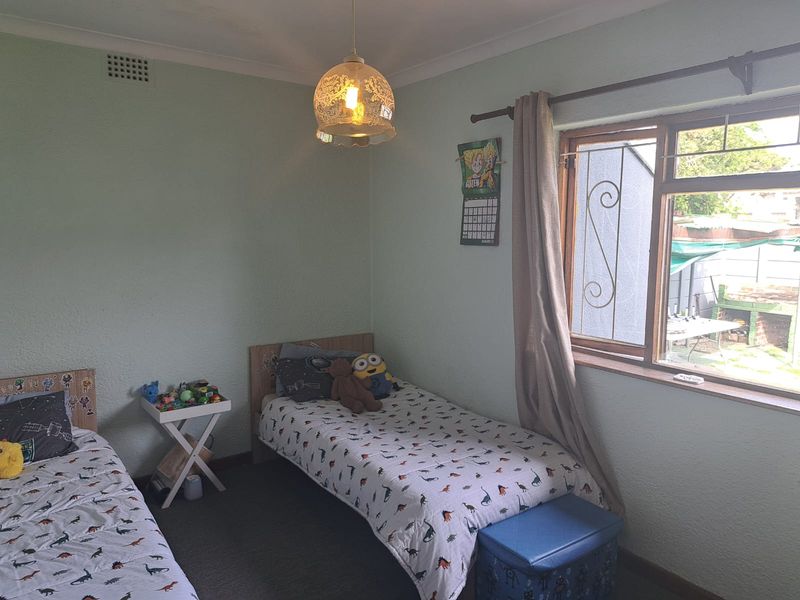 A functional bedroom featuring textured walls, coving, and a timber-framed window with security bars, offering a view of the rear garden area.