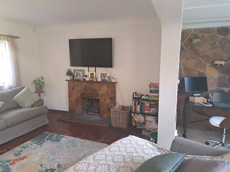 Living room featuring a rustic stone fireplace, classic parquet flooring, and an open-plan layout connecting to an adjacent study area.