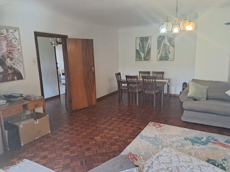 Spacious living and dining area featuring classic parquet flooring, a traditional chandelier, and a solid wood door leading to the adjacent room.