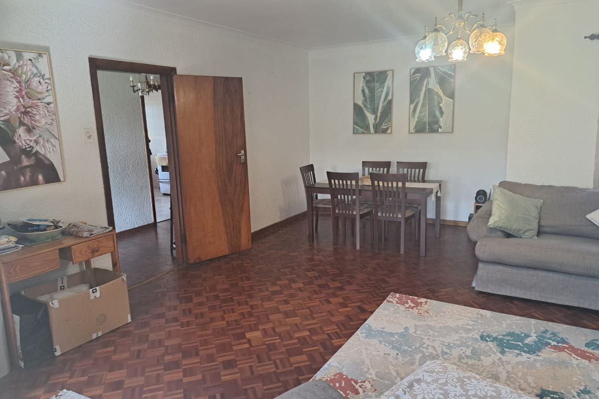 Spacious living and dining area featuring classic parquet flooring, a traditional chandelier, and a solid wood door leading to the adjacent room.