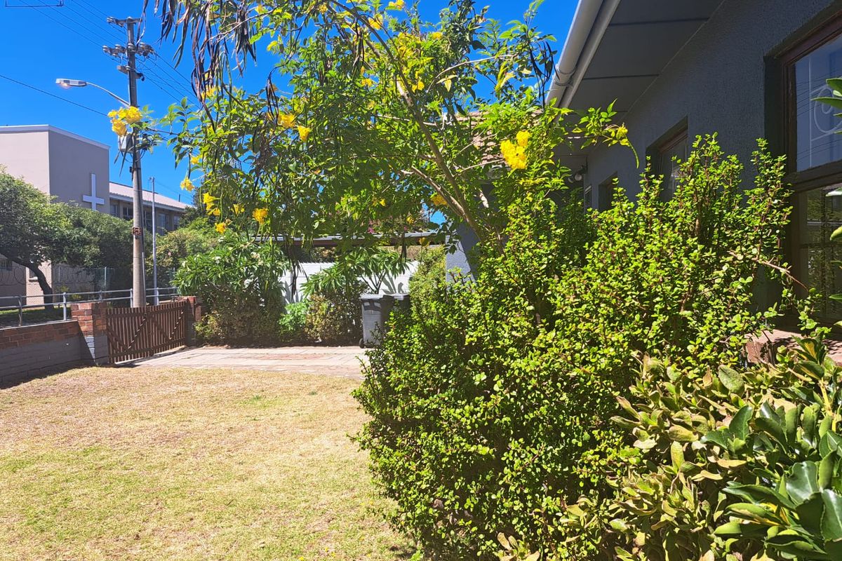 A rear garden area featuring a paved patio, established shrubs, and a timber gate leading to the street.