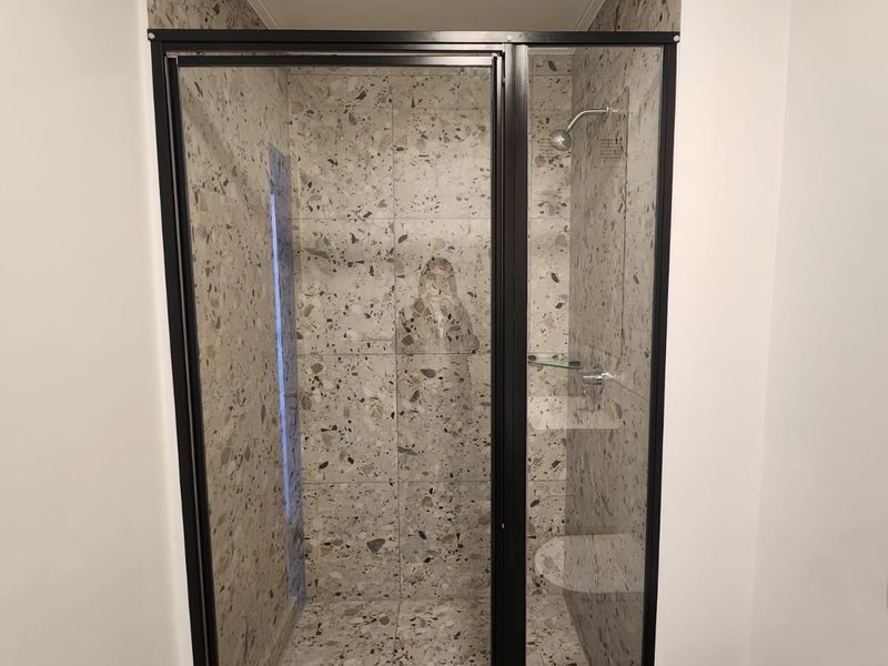 Modern bathroom featuring a walk-in shower with black-framed glass enclosure and stylish terrazzo-look tiling throughout.