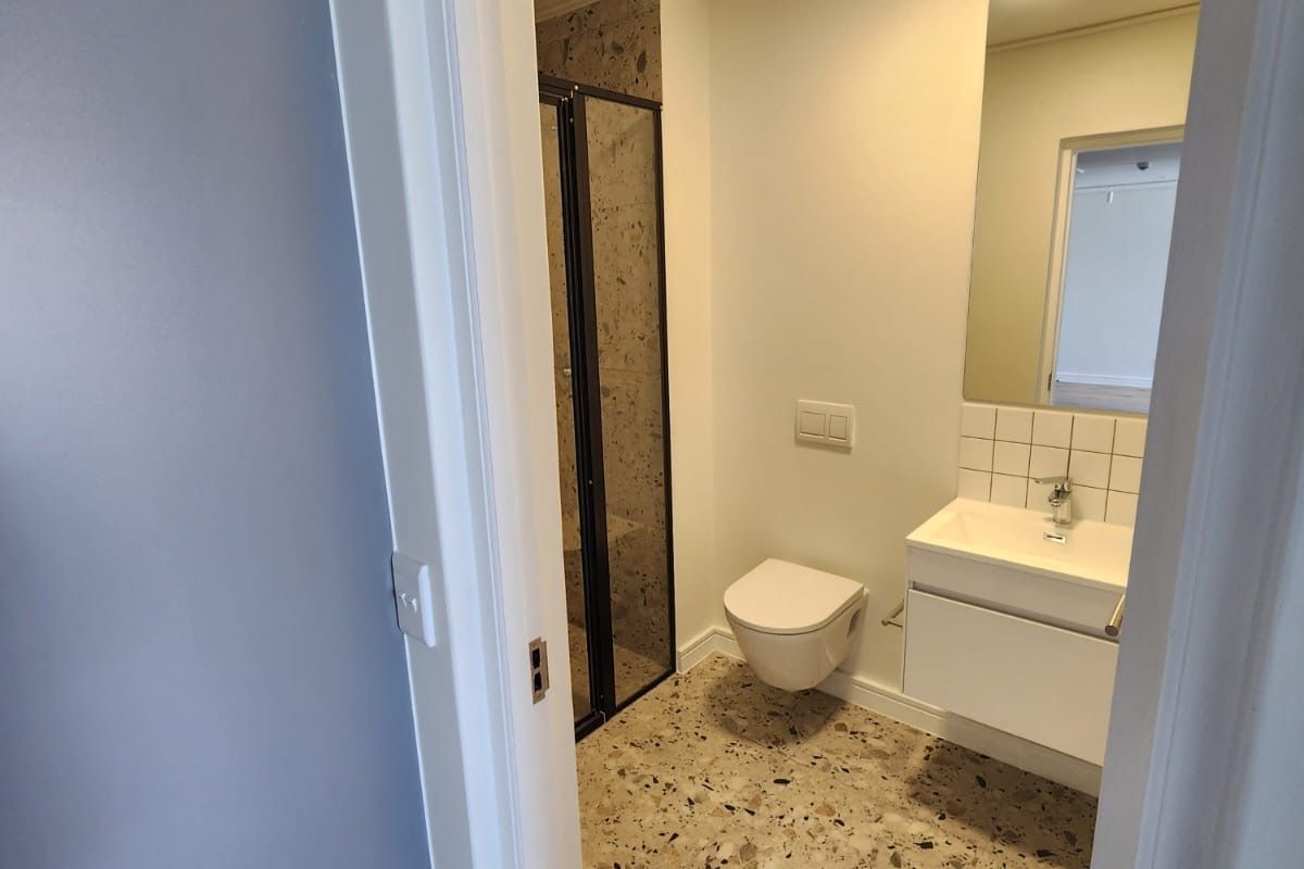 Modern bathroom featuring a wall-hung toilet, vanity with basin, and a walk-in shower with stylish terrazzo-style flooring.