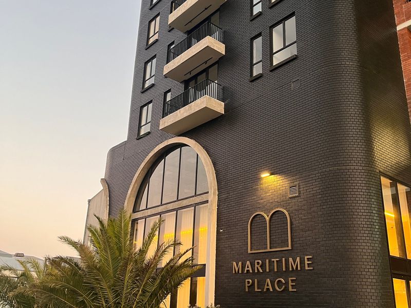 Modern multi-story apartment building facade featuring dark brickwork, arched architectural detailing, and private balconies.