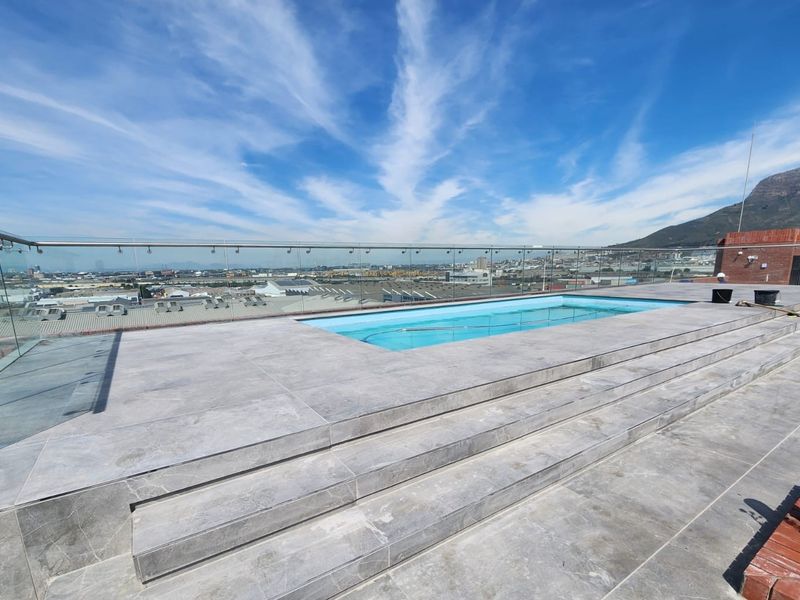 Rooftop swimming pool area featuring a modern glass balustrade, tiled decking, and panoramic mountain and city views.