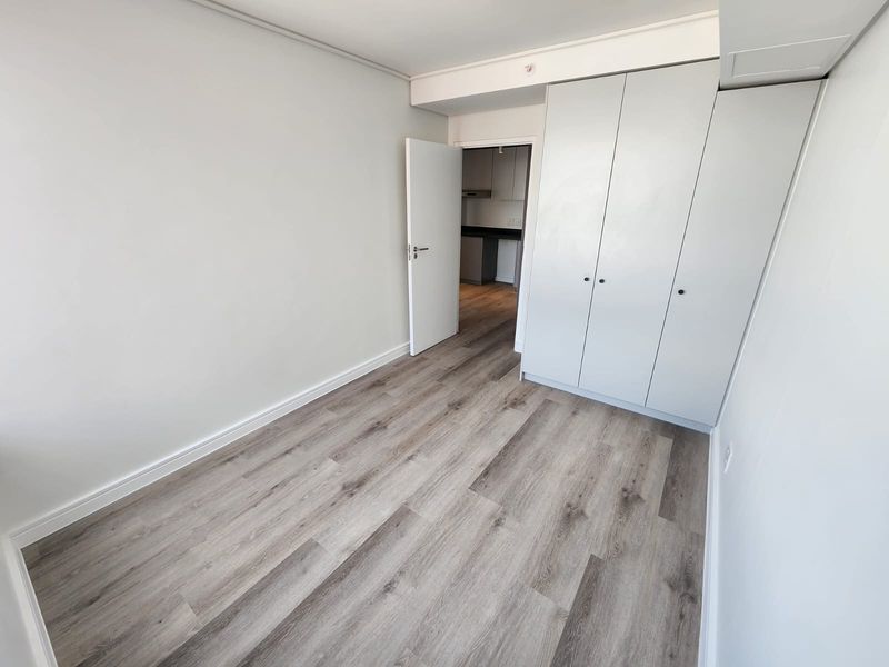 A bright, empty bedroom featuring modern light-toned laminate flooring and floor-to-ceiling built-in cupboards, offering a clean and neutral space ready for personalization.