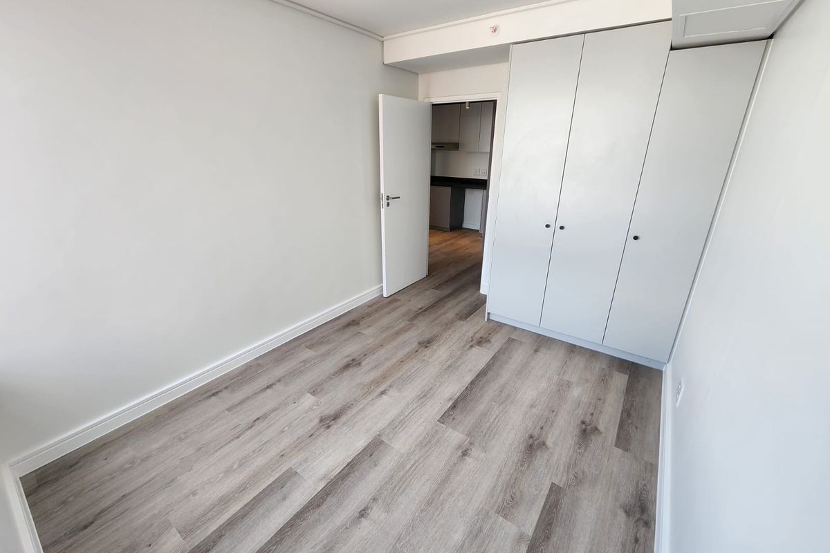 A bright, empty bedroom featuring modern light-toned laminate flooring and floor-to-ceiling built-in cupboards, offering a clean and neutral space ready for personalization.
