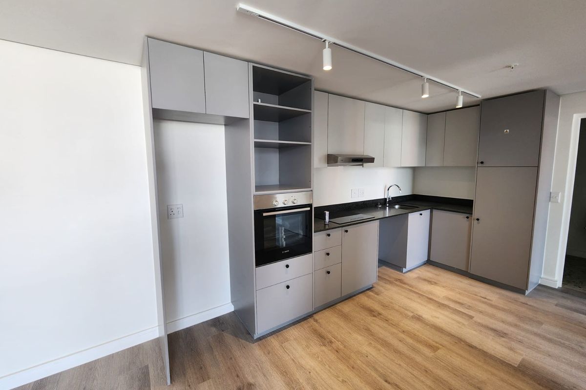 Modern kitchen featuring sleek grey cabinetry, built-in oven, extractor fan, dark stone countertops, and durable laminate flooring in an open-plan layout.