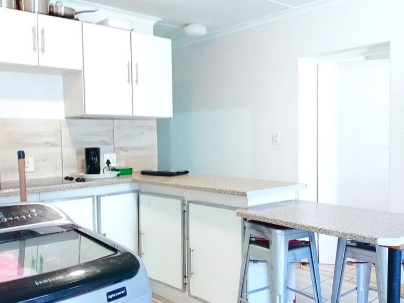 Functional kitchen featuring white cabinetry, laminate countertops, a tiled backsplash, and an integrated breakfast bar area.