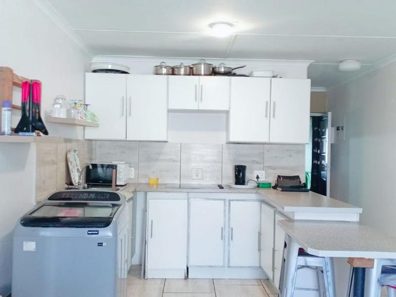 Compact kitchen featuring white cabinetry, laminate countertops, tiled backsplash, and an integrated breakfast bar, providing a functional layout for daily use.