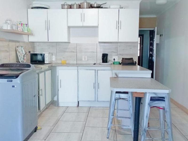 A functional kitchen featuring white cabinetry, laminate countertops, tiled backsplash, and a breakfast bar area with tiled flooring.