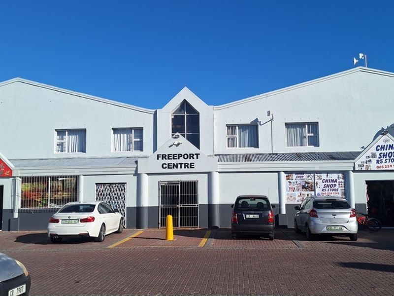 Front elevation of the Freeport Centre commercial building featuring multiple storefronts, security gates, and a paved parking area.