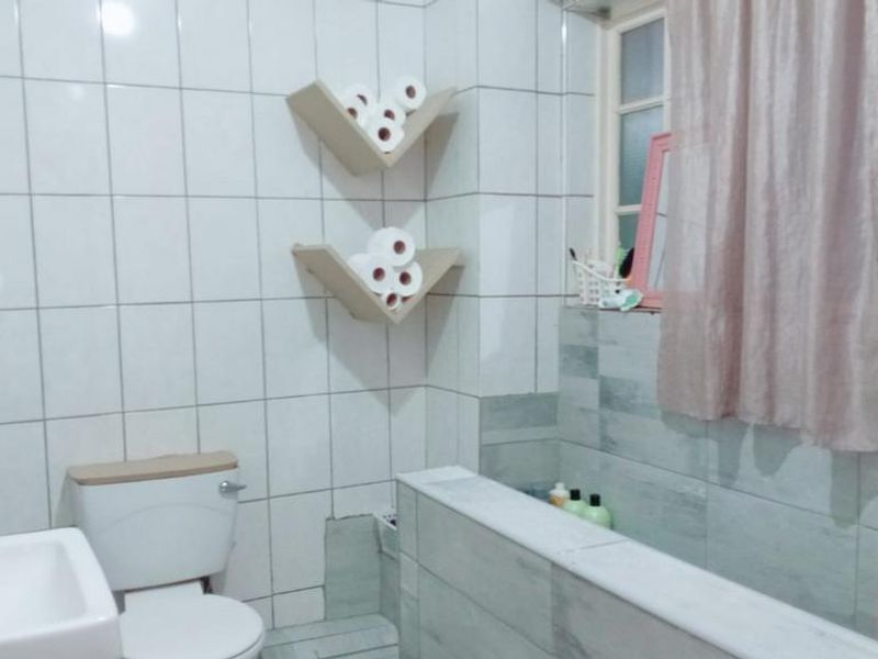 A functional bathroom featuring tiled walls, a built-in bathtub, and a standard toilet. The space requires some maintenance and cosmetic updates.
