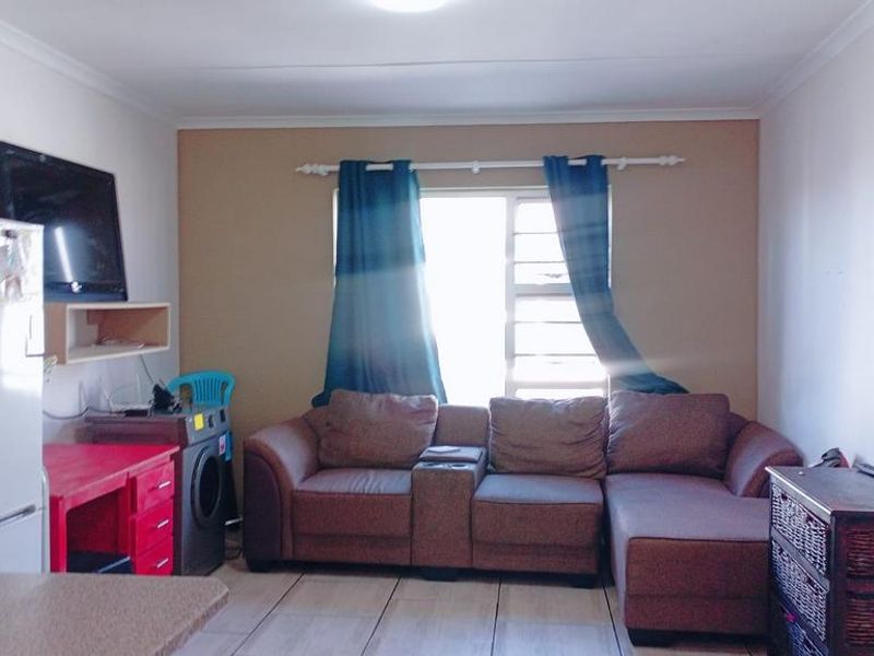 A functional living room area featuring tiled flooring, a window with security bars, and neutral wall finishes.