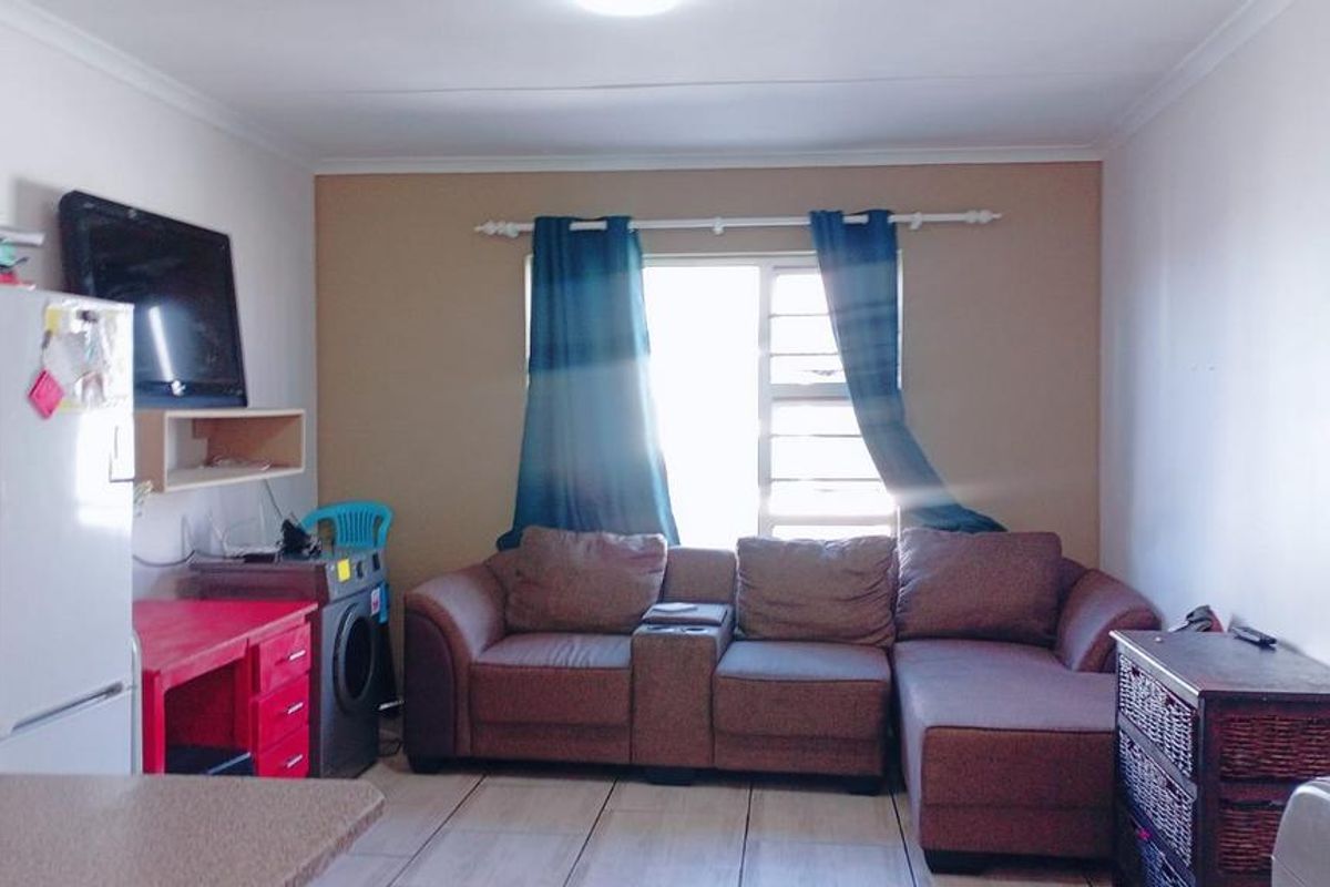 A functional living room area featuring tiled flooring, a window with security bars, and neutral wall finishes.