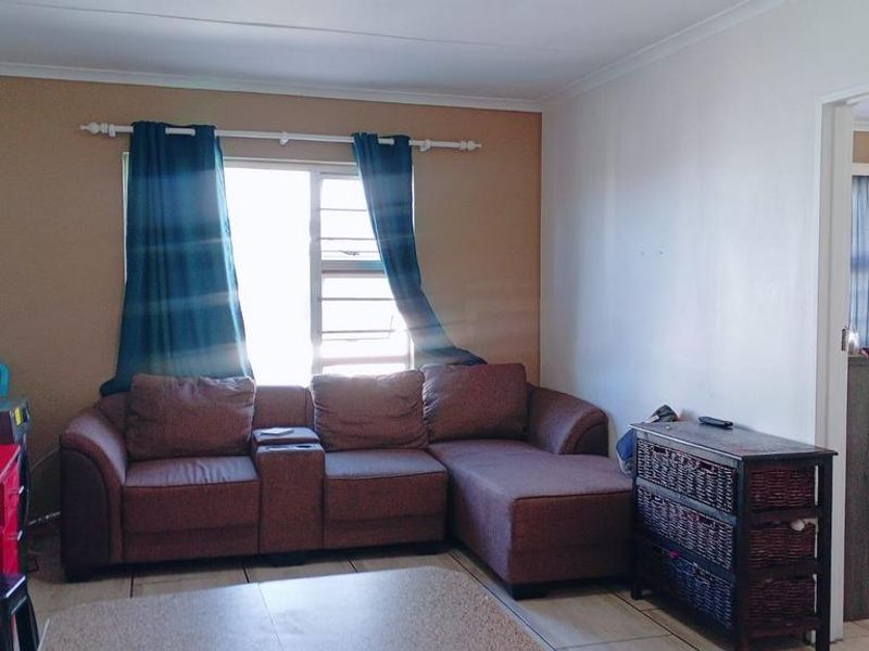 Open plan living area featuring tiled flooring and natural light through an aluminium window, with an adjacent view into a bedroom.