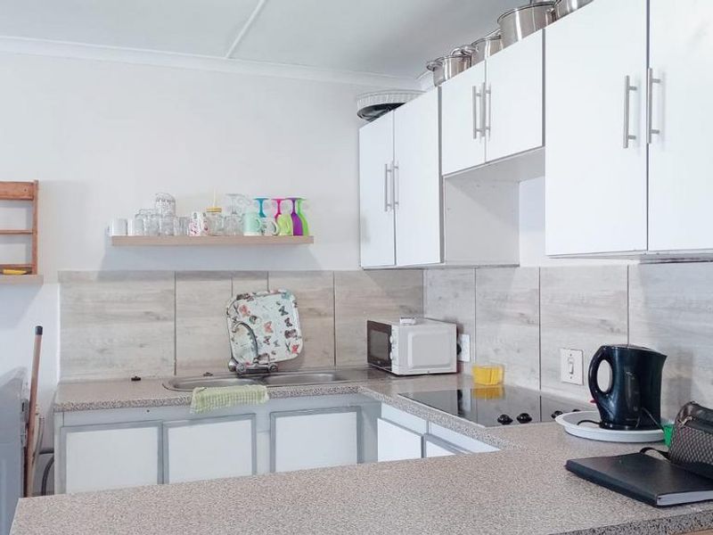 A functional kitchen featuring white cabinetry, laminate countertops, a tiled backsplash, and an integrated electric cooktop with ample storage space.