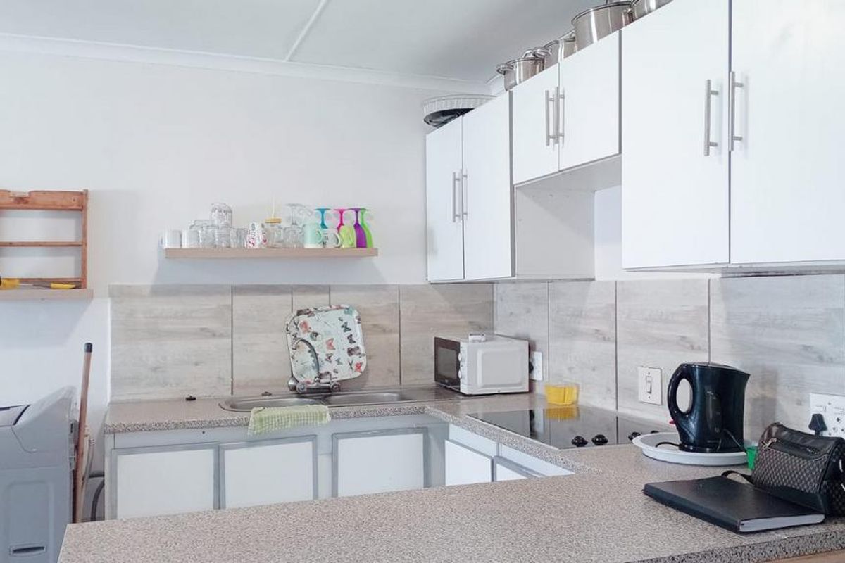 A functional kitchen featuring white cabinetry, laminate countertops, a tiled backsplash, and an integrated electric cooktop with ample storage space.