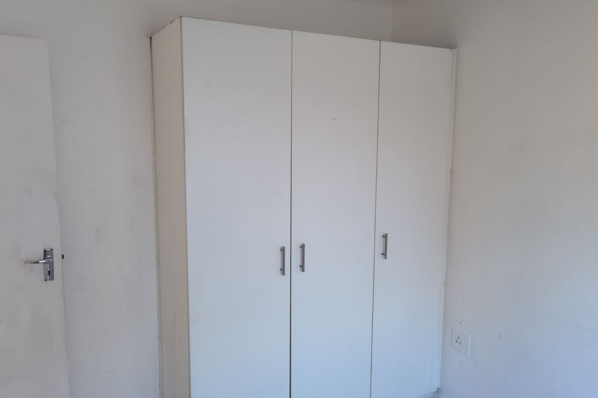 A bedroom featuring a white built-in wardrobe with modern handles, set against plain walls with a standard electrical outlet.