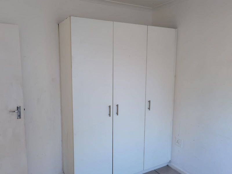 A bedroom featuring a white built-in wardrobe with modern handles, set against plain walls with a standard electrical outlet.