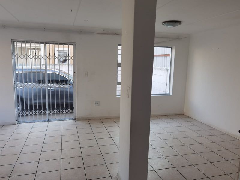 An empty, open-plan living area featuring tiled flooring, a central structural column, and a sliding door with a security gate.