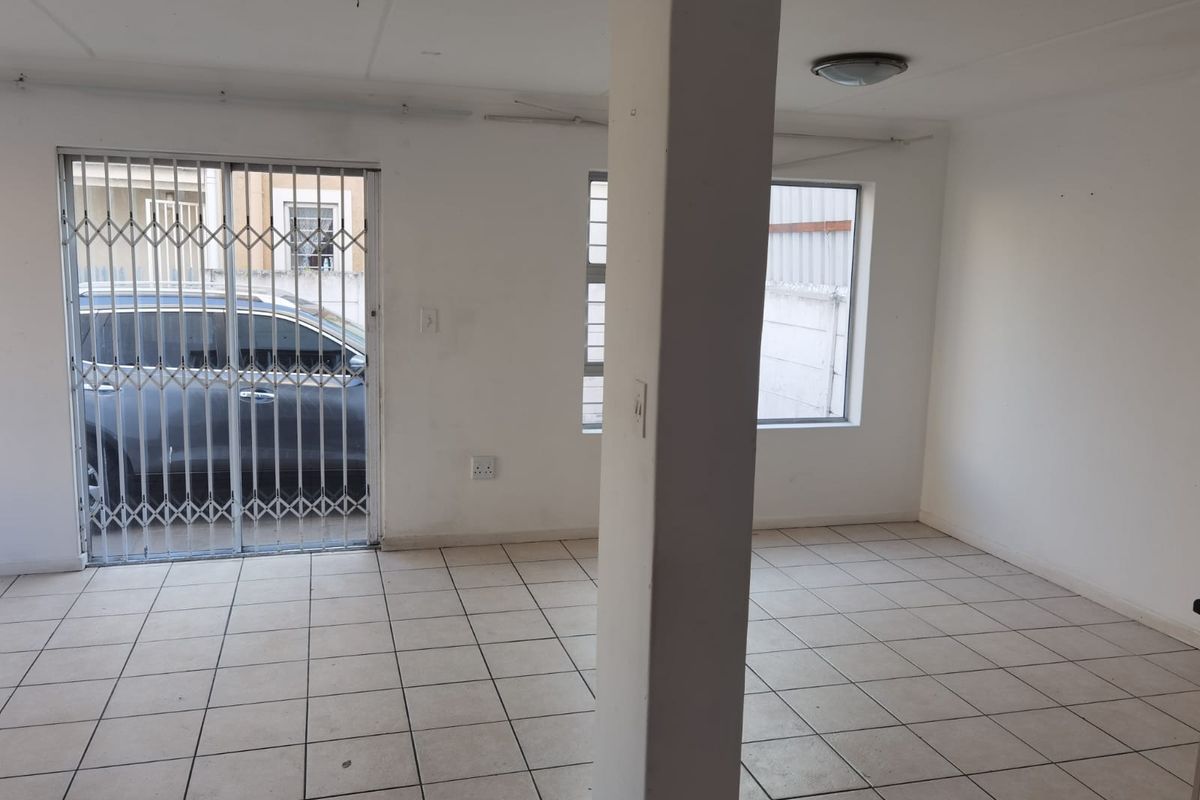 An empty, open-plan living area featuring tiled flooring, a central structural column, and a sliding door with a security gate.