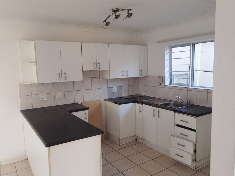 A functional kitchen featuring white cabinetry, dark laminate countertops, tiled backsplash, and tiled flooring, currently vacant and ready for renovation.
