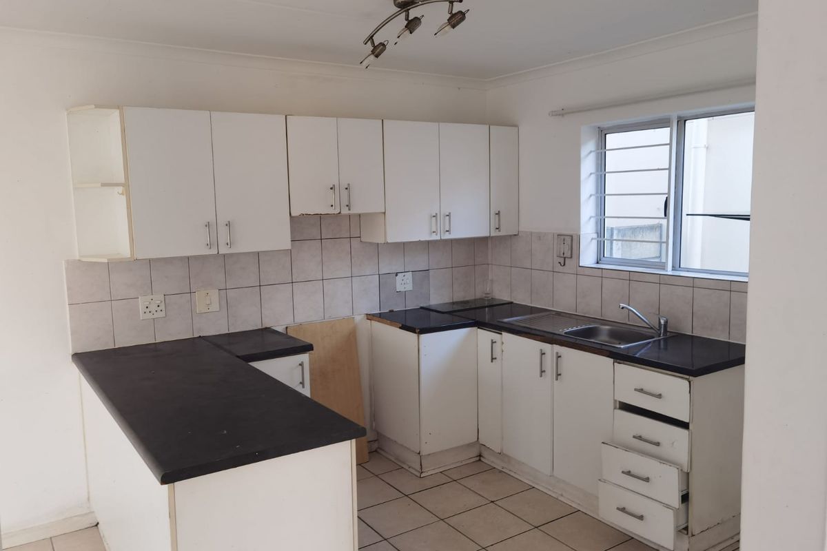 A functional kitchen featuring white cabinetry, dark laminate countertops, tiled backsplash, and tiled flooring, currently vacant and ready for renovation.