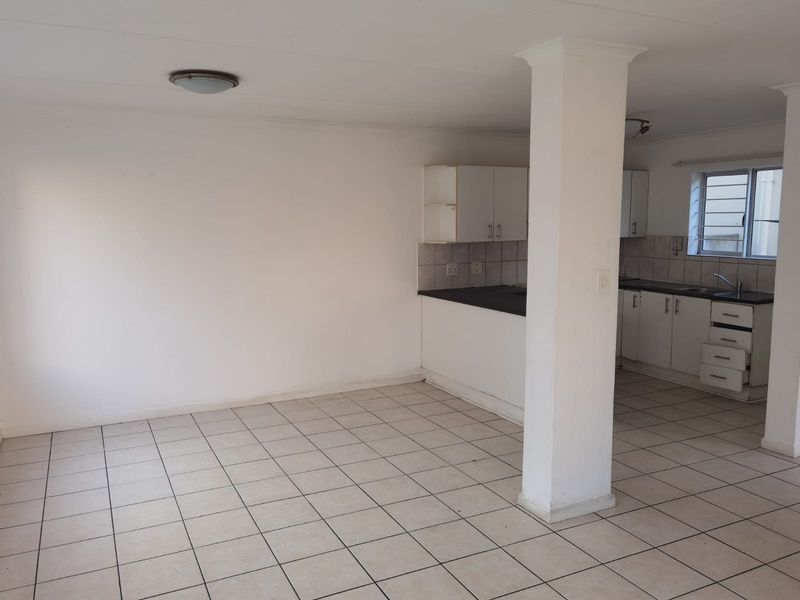 Open-plan kitchen and living area featuring tiled flooring, white cabinetry, and a central structural column, offering a functional blank canvas for renovation.