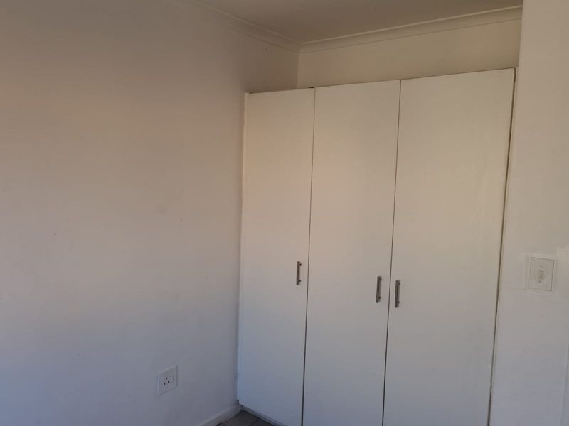 A simple bedroom interior featuring a white built-in wardrobe and plain wall finishes.