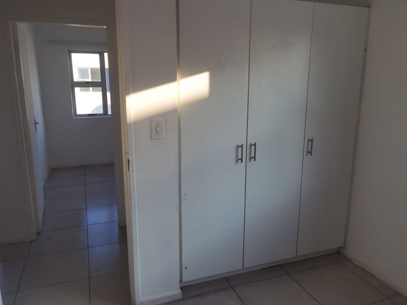 A simple, empty bedroom featuring built-in cupboards, tiled flooring, and a view through to an adjacent room.