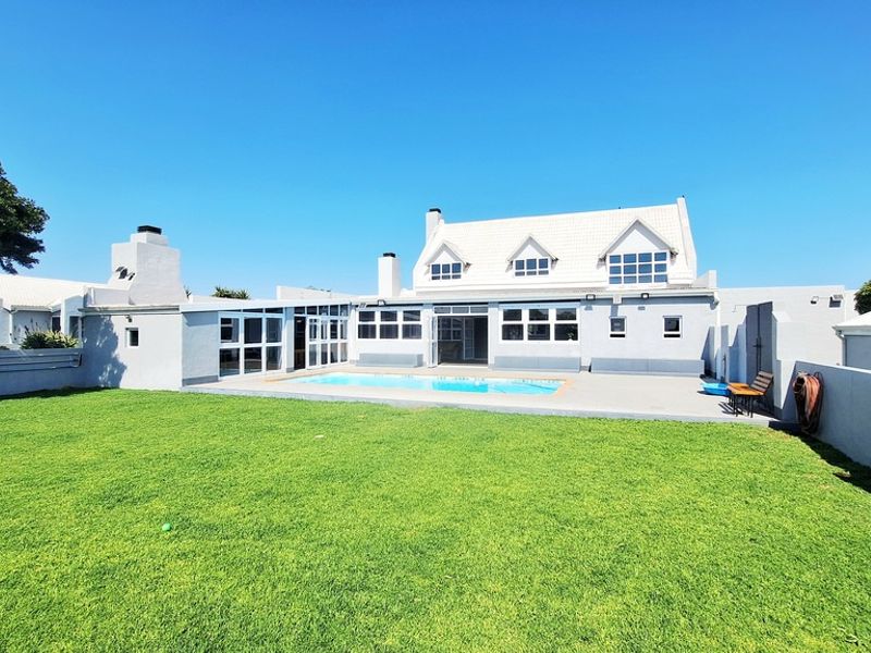 Rear view of the property featuring a well-maintained lawn, a swimming pool, and a paved patio area leading to the main dwelling.