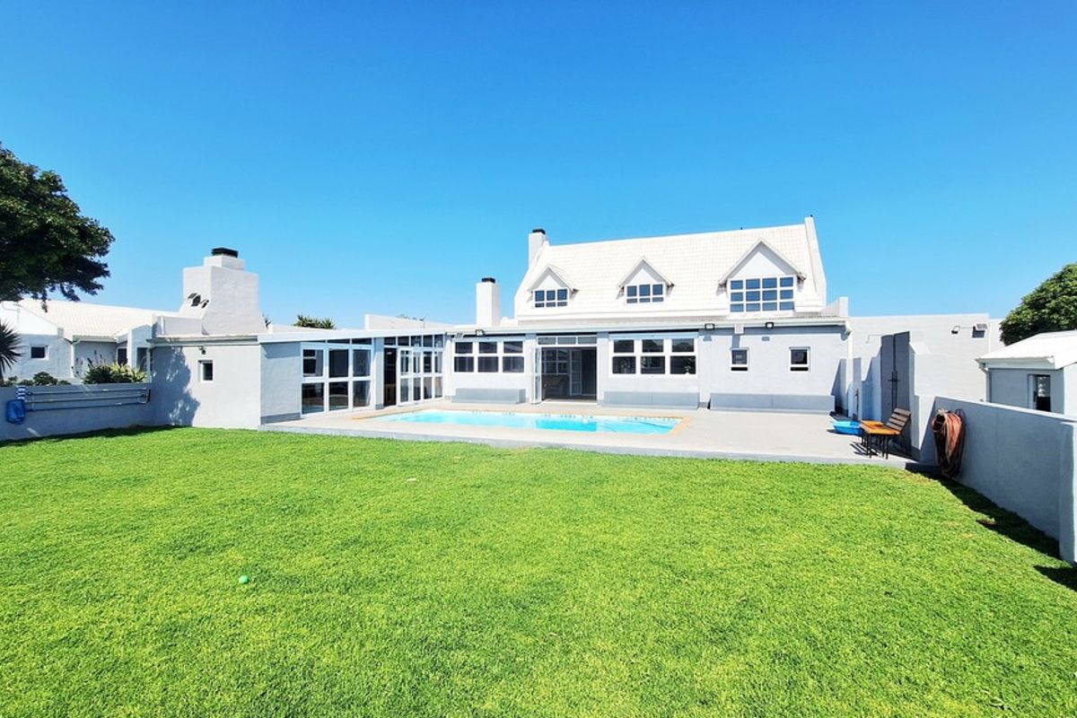 Rear view of the property featuring a well-maintained lawn, a swimming pool, and a paved patio area leading to the main dwelling.