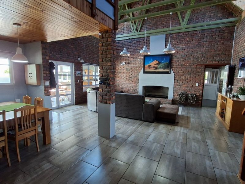 Spacious open-plan living and dining area featuring exposed brick walls, high timber ceilings with exposed trusses, and a central fireplace.