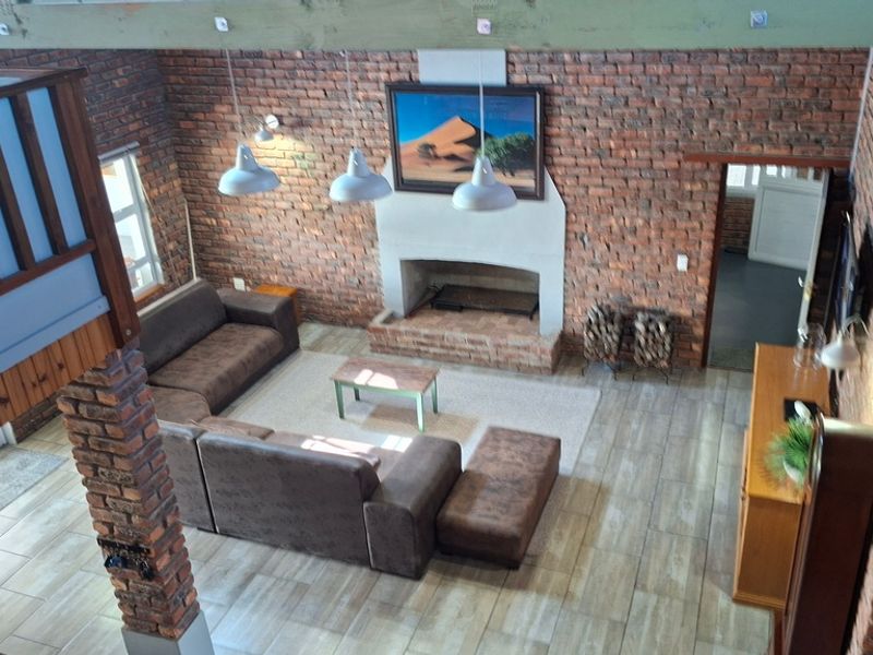 Spacious double-volume living area featuring exposed brick walls, a central fireplace, tiled flooring, and a mezzanine level with timber railings.