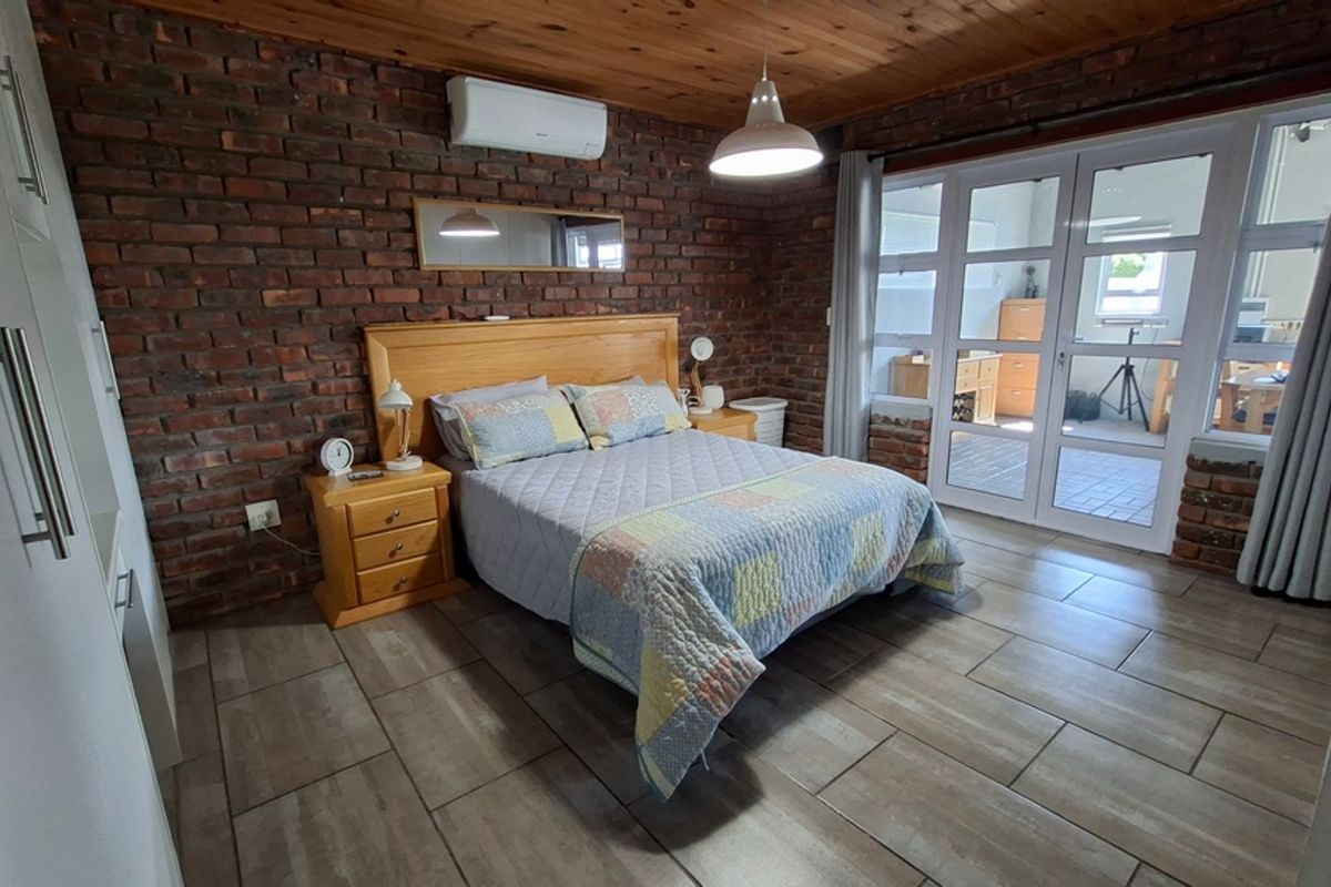 Spacious bedroom featuring exposed brick walls, timber ceiling, tiled flooring, and large glass sliding doors providing natural light and access to the patio.