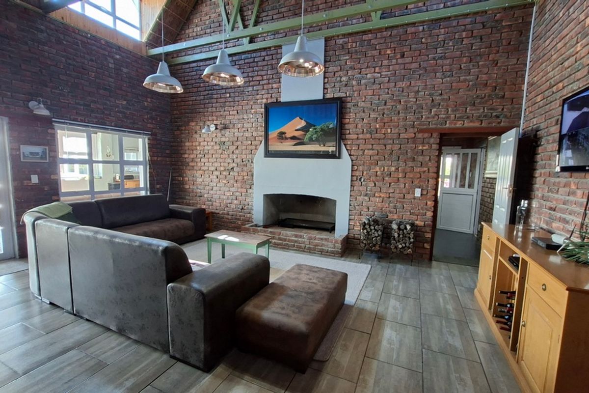 Spacious living room featuring exposed brick walls, vaulted ceilings with timber trusses, tiled flooring, and a central masonry fireplace.