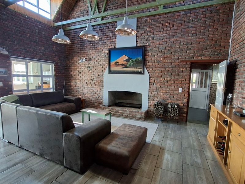 Spacious living room featuring exposed brick walls, vaulted ceilings with timber trusses, tiled flooring, and a central masonry fireplace.