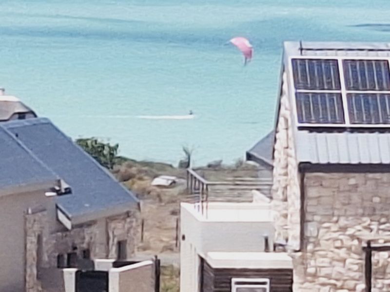Elevated view of residential properties featuring stone cladding and solar panel installations, overlooking the ocean.