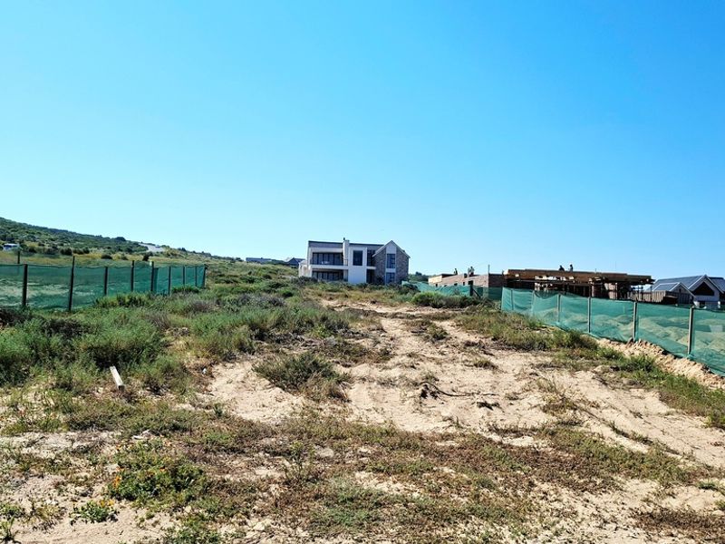 A vacant residential plot of land featuring natural vegetation and perimeter fencing, situated in a developing coastal or estate area.