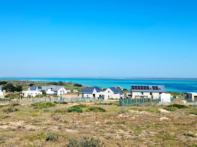 An elevated view of a coastal residential development featuring modern homes with metal roofs and solar panels overlooking the ocean.
