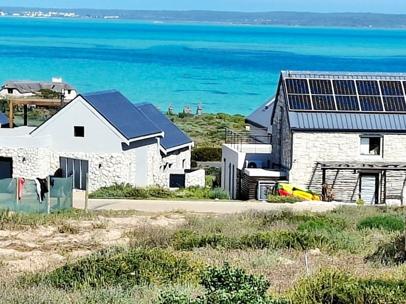 A scenic view of coastal residential properties featuring stone-clad exteriors, metal roofing, and integrated solar panels overlooking the turquoise ocean.