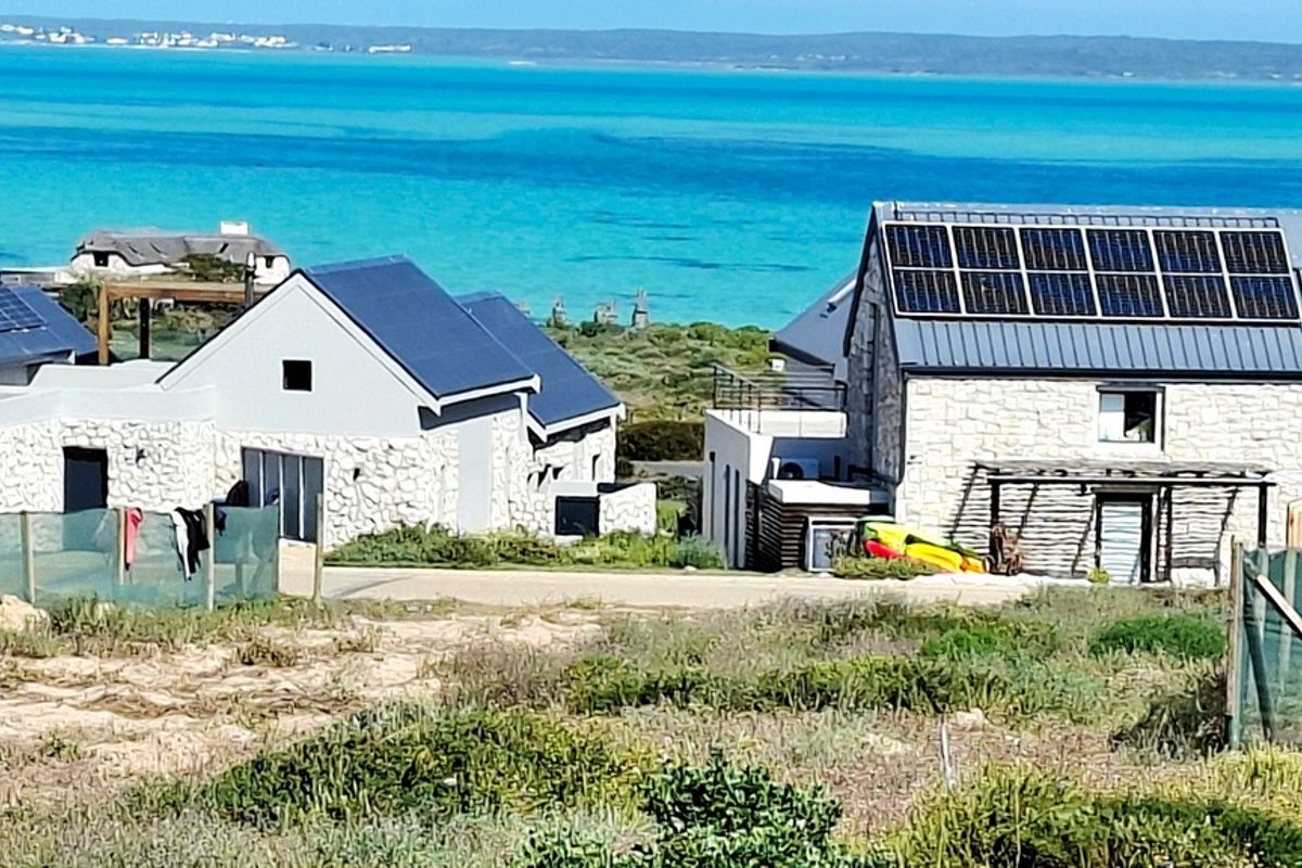 A scenic view of coastal residential properties featuring stone-clad exteriors, metal roofing, and integrated solar panels overlooking the turquoise ocean.