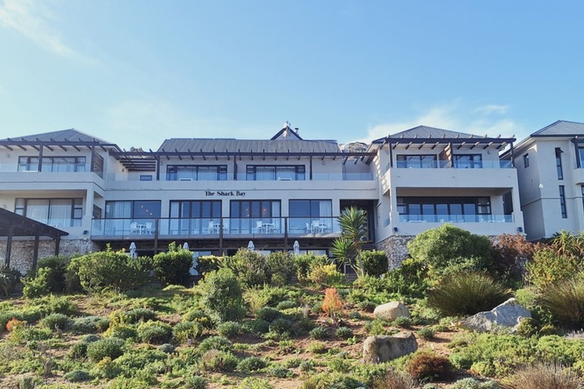 A well-maintained multi-level residential building featuring glass balustrades, timber pergolas, and extensive sliding doors overlooking a landscaped garden.