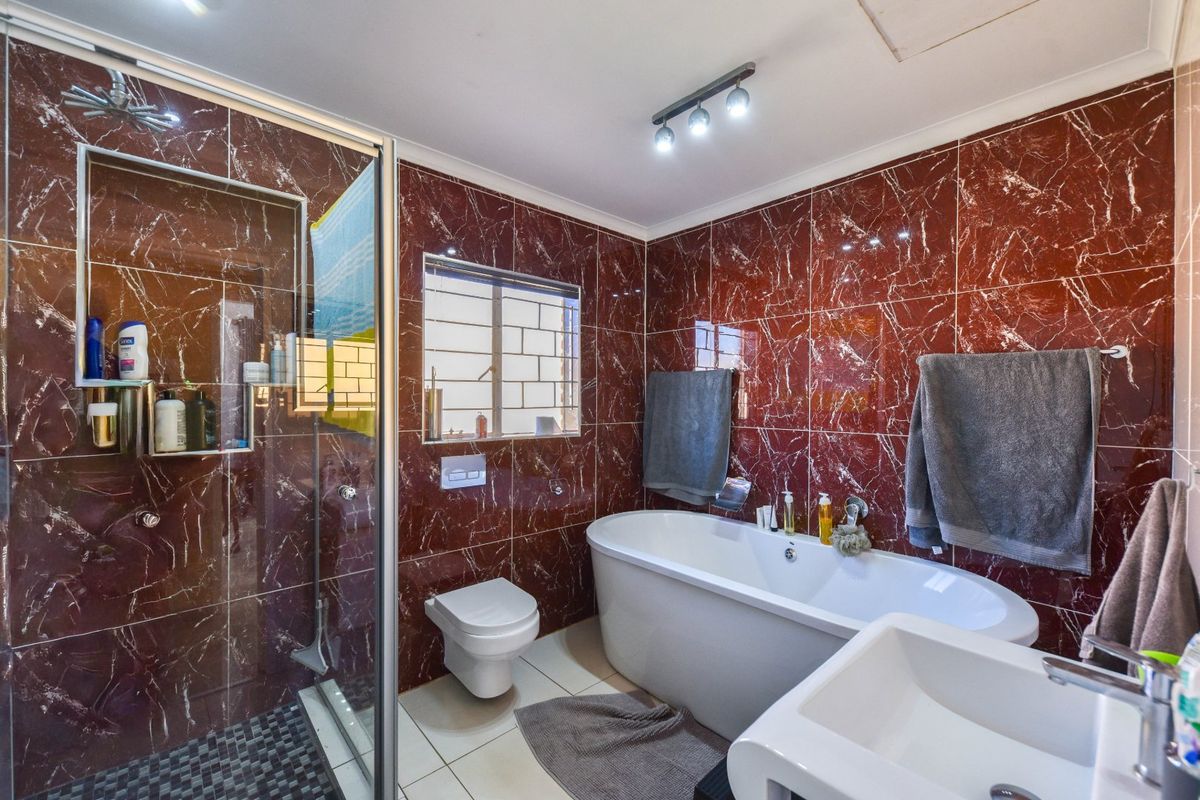 A bathroom featuring dark red marble-style wall tiles, a freestanding bathtub, a glass-enclosed shower, and a wall-mounted toilet.